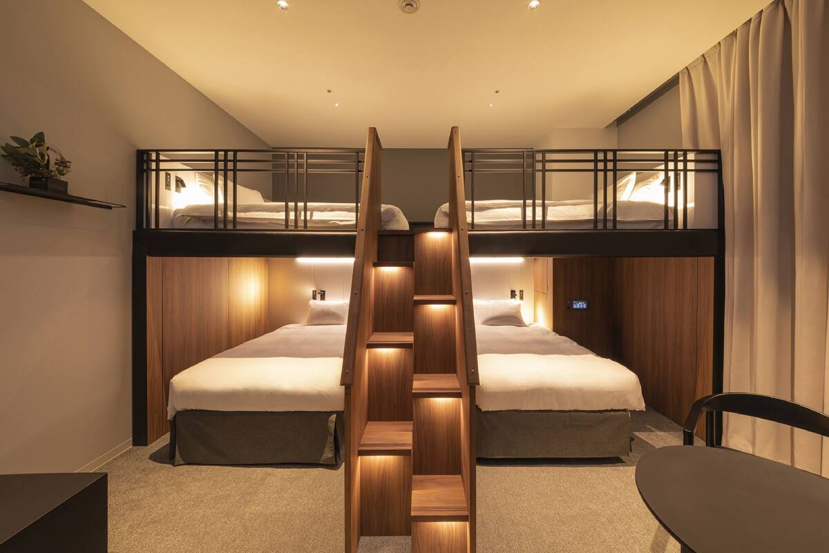 Une chambre d’hôtel avec deux lits superposés, une échelle en bois, un bureau et une chaise.