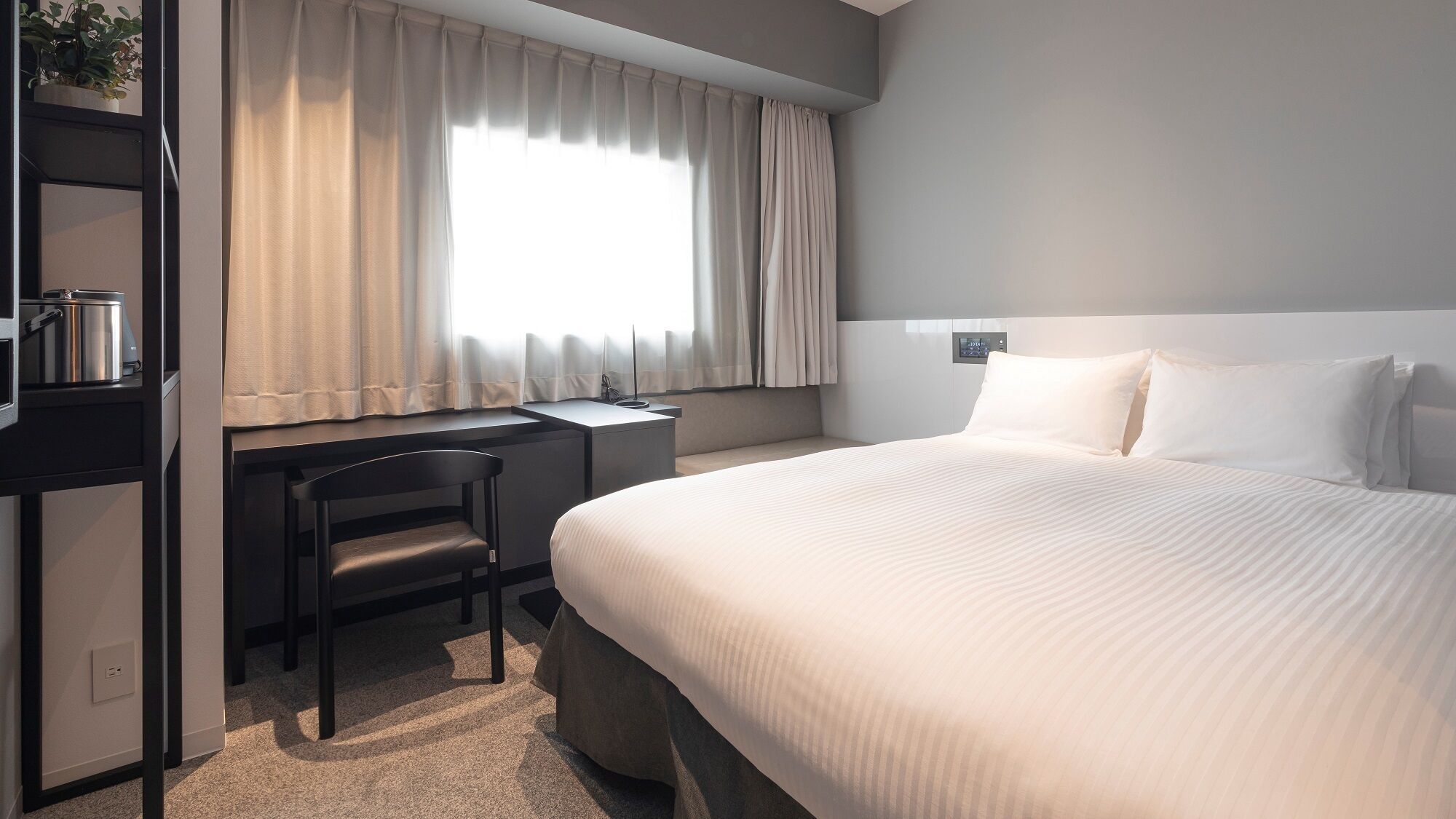 Een hotelkamer met een bed, een bureau, een stoel en een raam met gordijnen.
