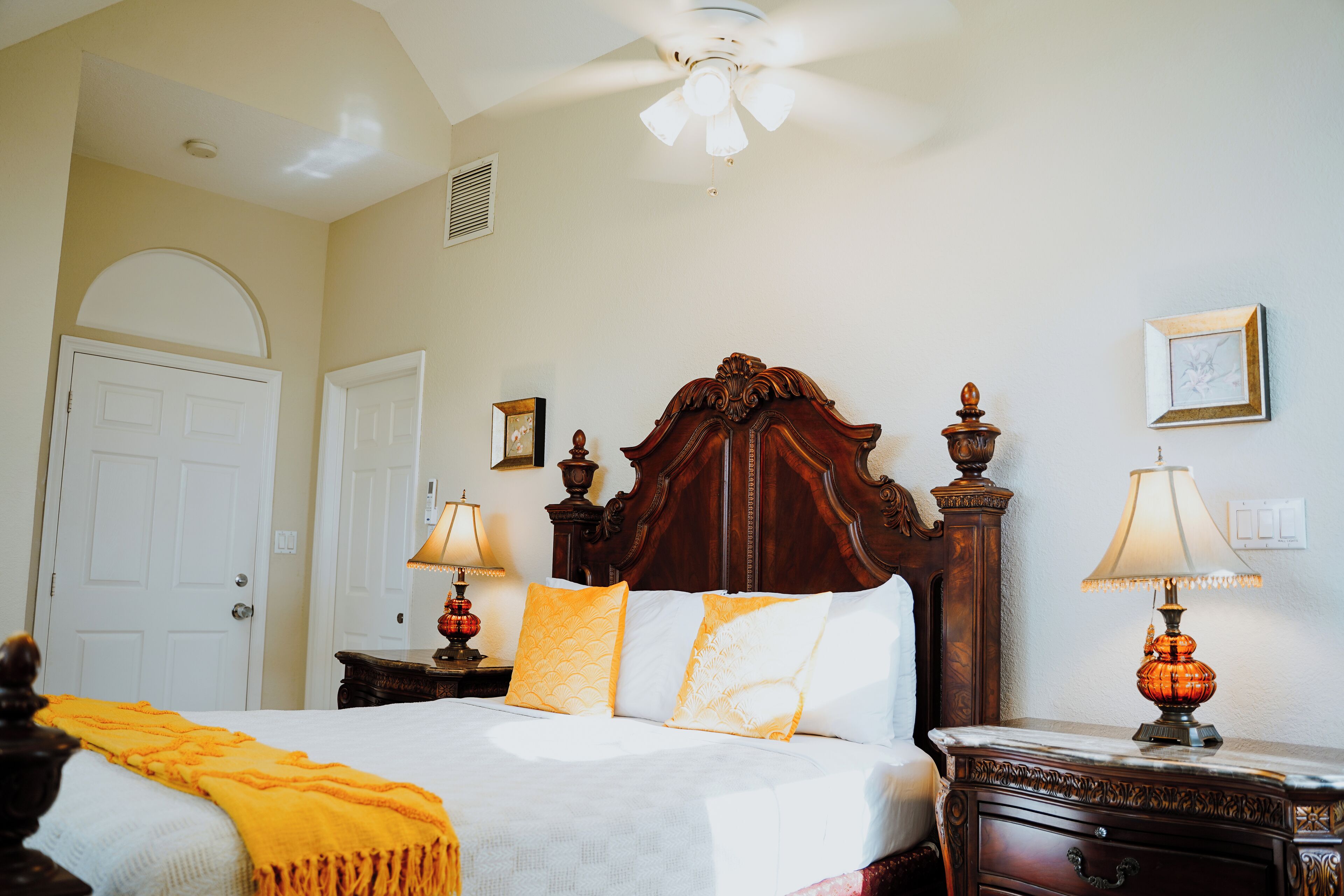 A hotel room with a large bed, two bedside tables with lamps, a ceiling fan, and a door.