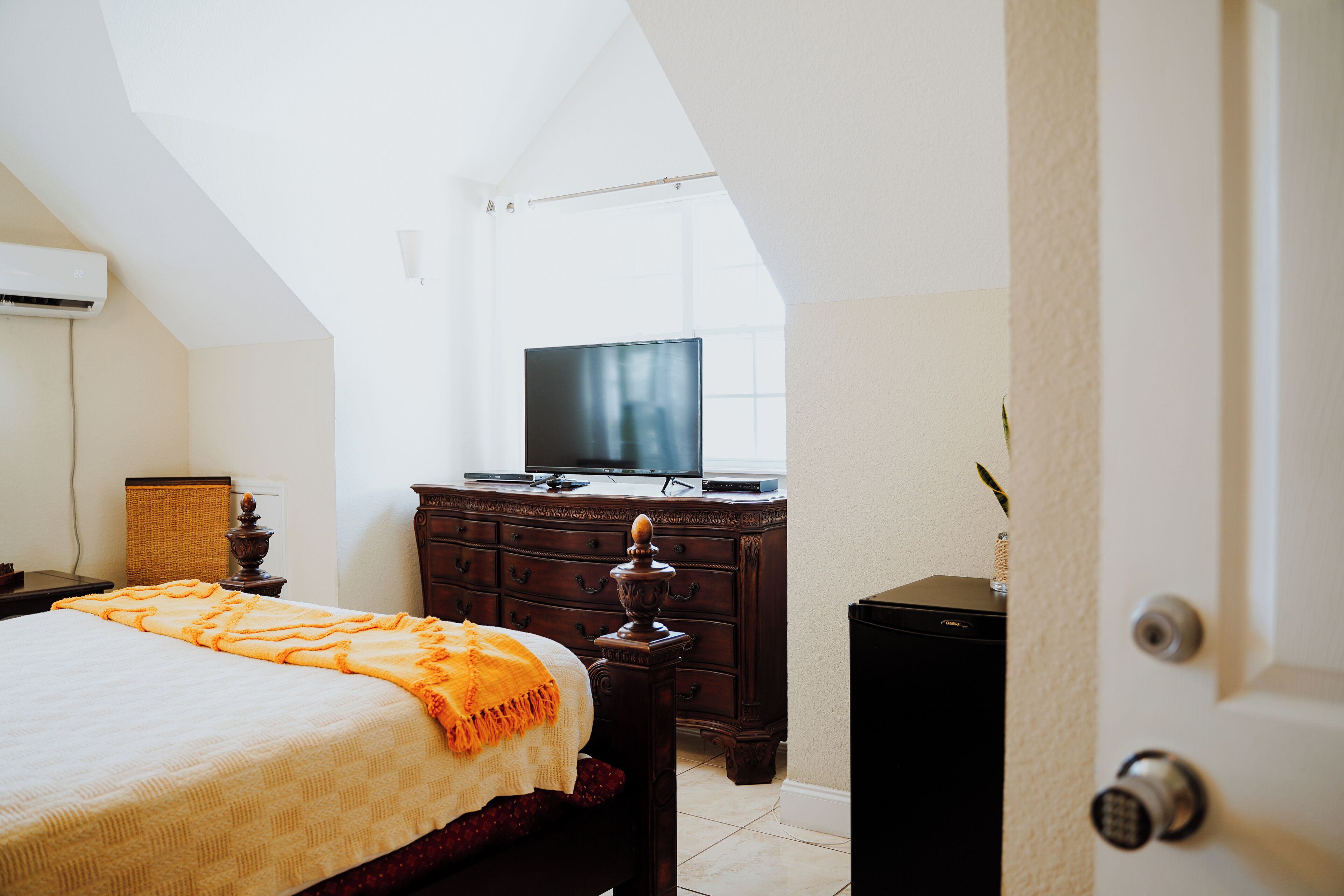 A bedroom with a bed, a dresser, a television, and a door.