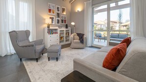 Ein Wohnzimmer mit einer Couch, Sesseln, einem Schrank und einem großen Fenster.