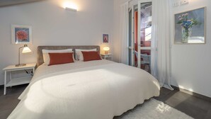 Ein Schlafzimmer mit einem großen Bett, zwei Nachttischen mit Lampen, einem Fenster mit Vorhängen und einem Gemälde an der Wand.