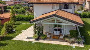 Ein zweistöckiges Haus mit Ziegeldach, einer überdachten Terrasse mit Gartenmöbeln und einem gepflegten Rasen.