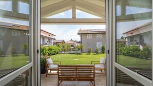 Eine Terrasse mit einer Holzbank und Stühlen, einer Glastür und Blick auf Nachbarhäuser.