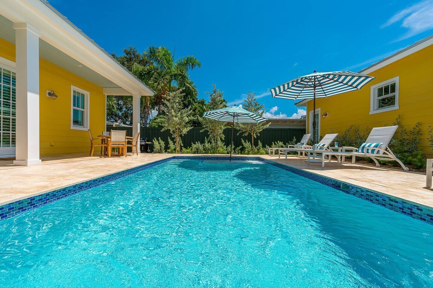 A swimming pool with lounge chairs and umbrellas, surrounded by yellow walls and greenery.
