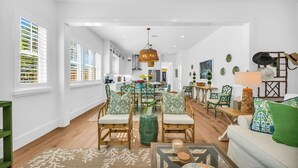 Un amplio salón con sofá, sillas y una mesa de centro. Se aprecia una cocina al fondo con una mesa de comedor y sillas.
