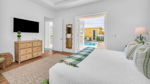 Un dormitorio con cama, televisor, cómoda y vista a una piscina exterior.
