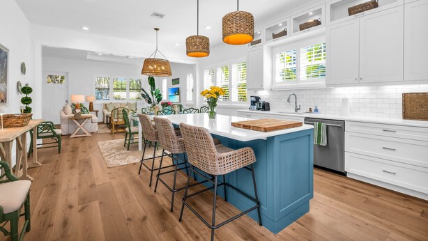 Una cocina moderna con armarios blancos, una isla azul, lámparas colgantes de mimbre y suelo de madera.