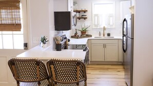 Una cocina moderna con una isla central, dos sillas de mimbre, un televisor de pantalla plana y un refrigerador de acero inoxidable.