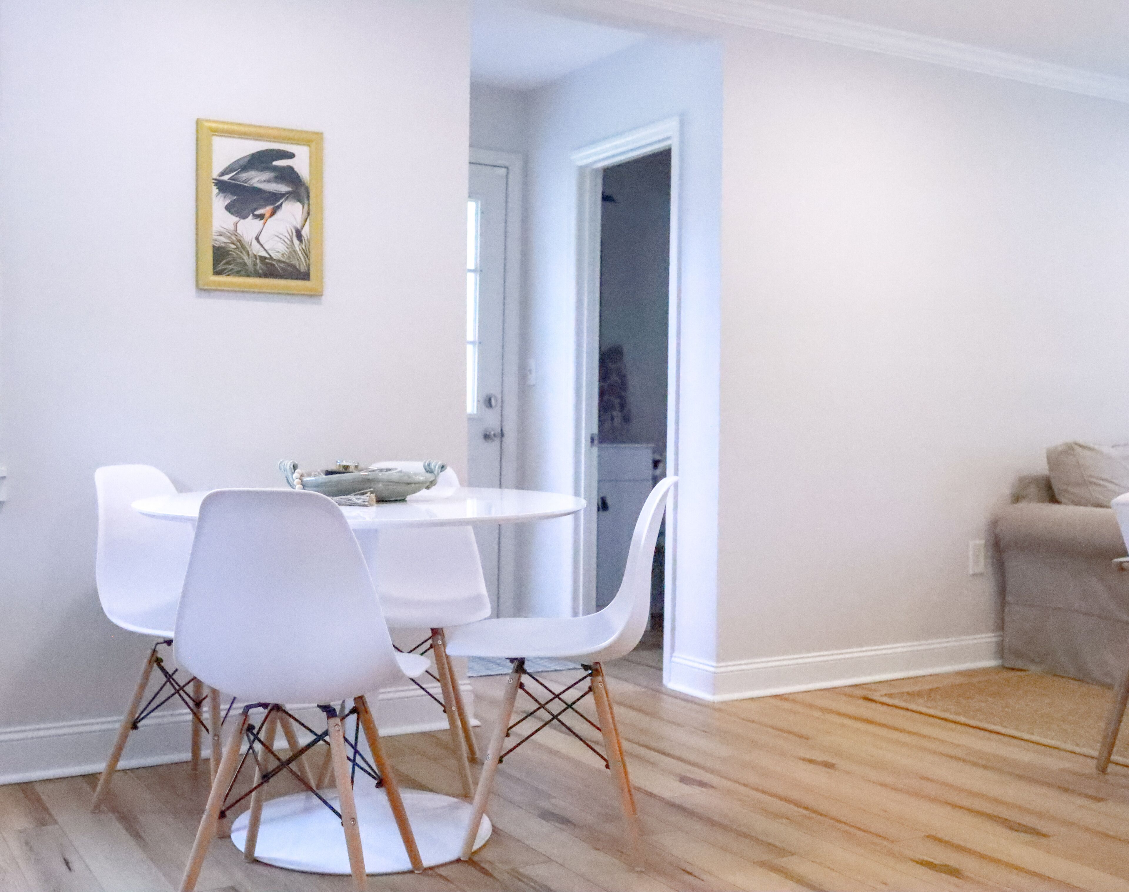 A dining area with a round table and white chairs, a framed picture on the wall, and a wooden floor.