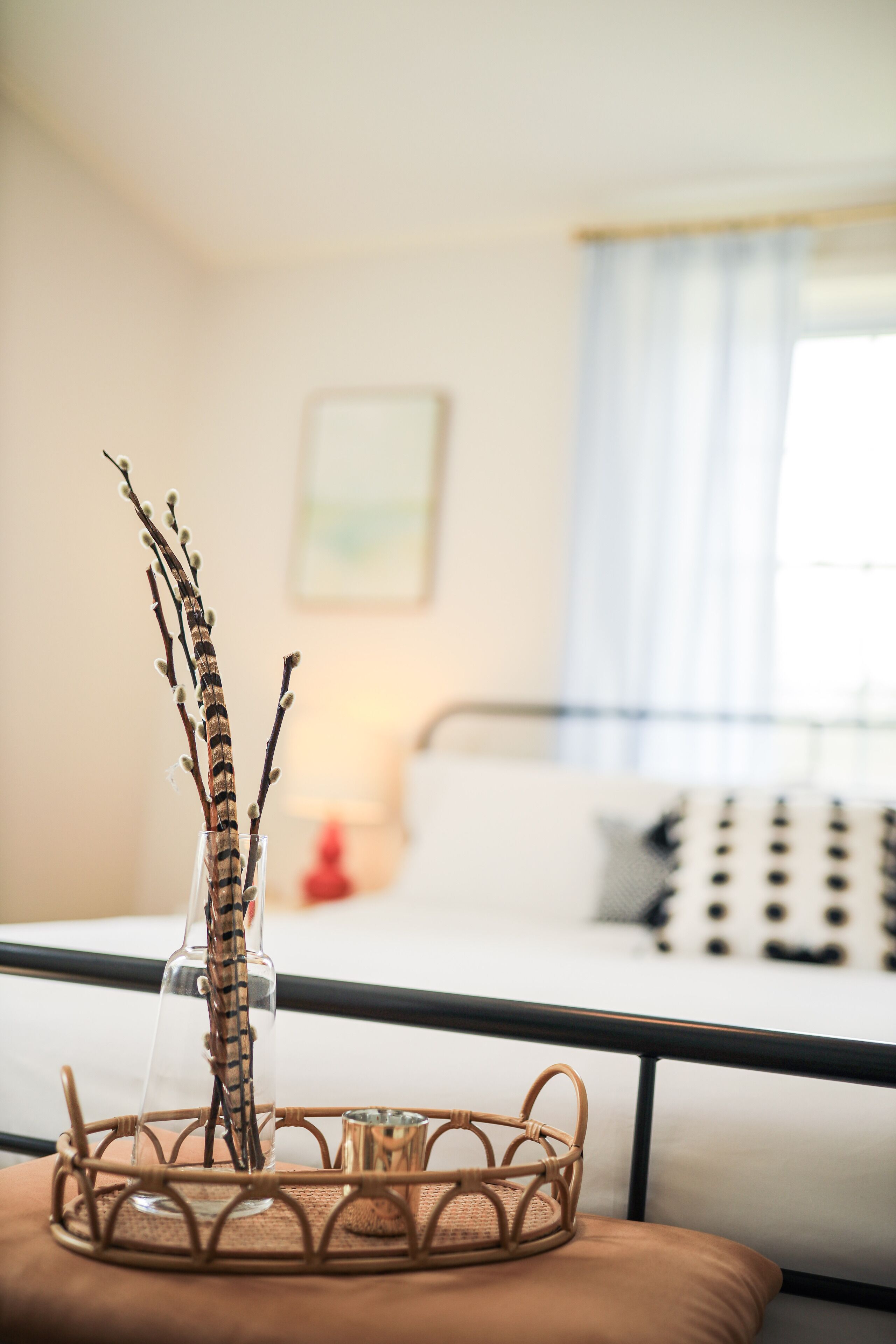 A room with a bed, a bedside table, and a wicker basket with branches.