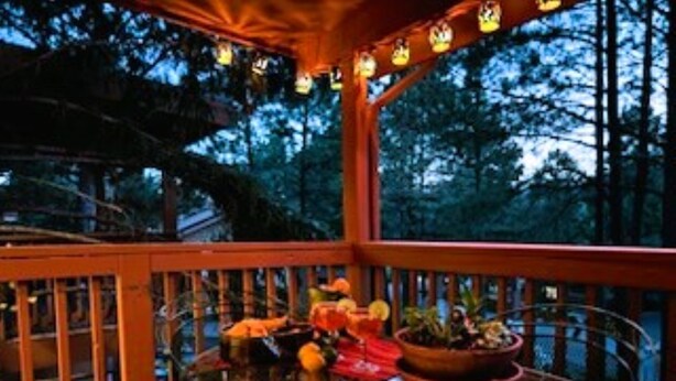 A glass-enclosed outdoor area with a wooden deck, potted plants, and a seating arrangement. - Xterra Championship Availability, Game Room, Sleeps 10 and Pet Friendly! (Ruidoso)