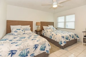 A room with two beds, each with a headboard and a nightstand with a lamp.