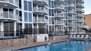 Un edificio moderno con varios balcones y una piscina con sillones de descanso.