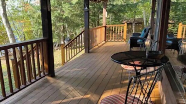 Une terrasse en bois avec une table et des chaises, entourée d’une rambarde.