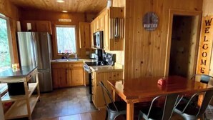 L’intérieur d’un chalet en bois comprend une cuisine, un coin repas et une pancarte sur laquelle on peut lire « BIENVENUE ».