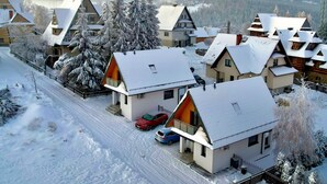Un village enneigé, avec des maisons traditionnelles, un ciel dégagé et des montagnes en arrière-plan.