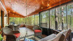 Une terrasse en bois, dotée de meubles en osier et d’un hamac, qui offre une vue sur une forêt.