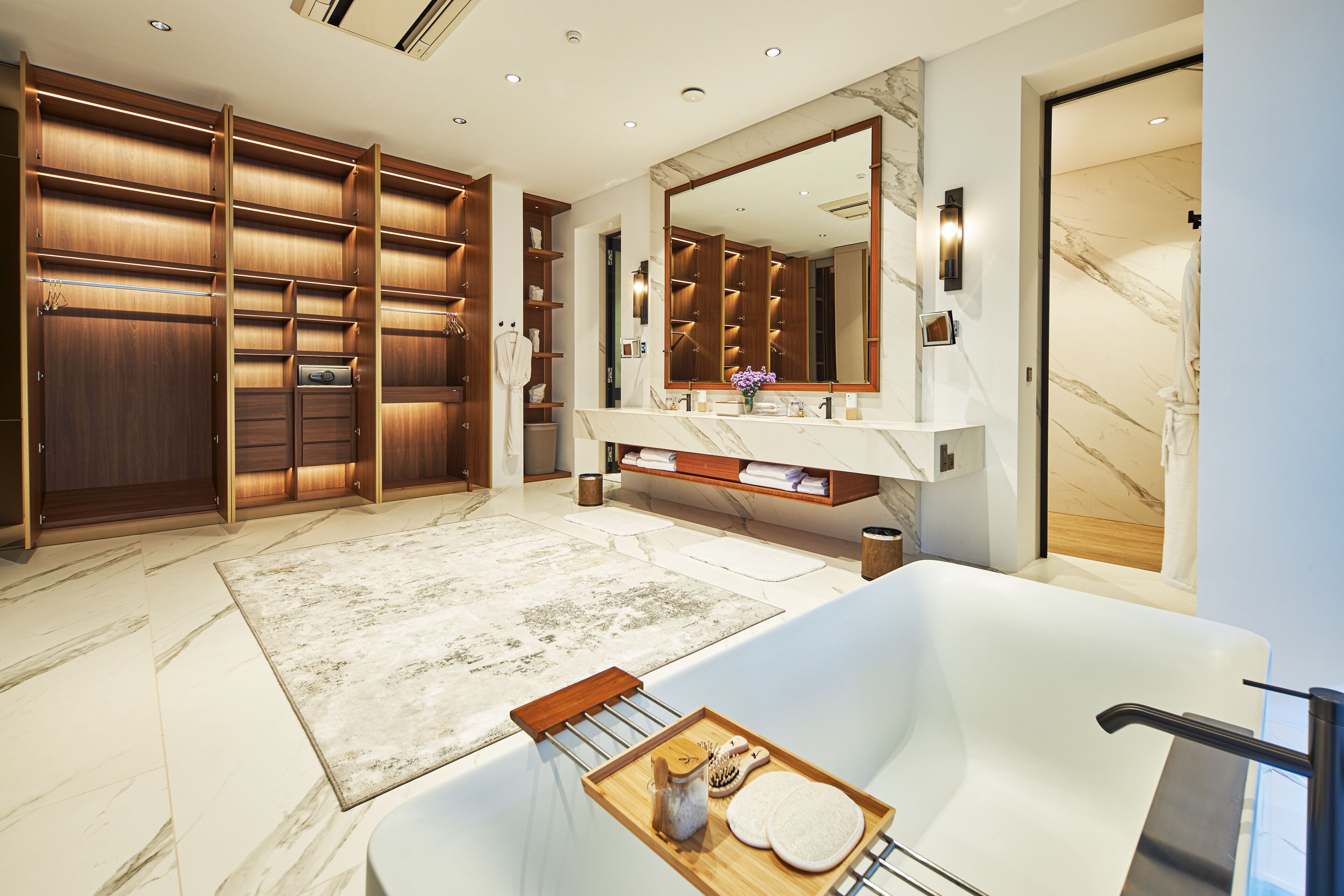A luxurious bathroom with a large mirror, marble flooring, a bathtub, and a wooden vanity.
