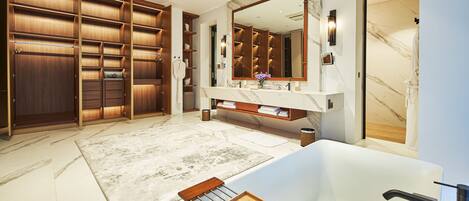 A luxurious bathroom with a large mirror, marble flooring, a bathtub, and a wooden vanity.
