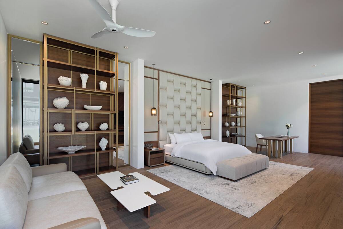 A modern bedroom with a bed, a sofa, a coffee table, a desk, and built-in shelving with decorative items.