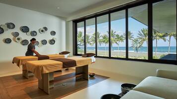 Relax in a serene spa room with a stunning beach view, featuring two massage tables and a peaceful atmosphere.