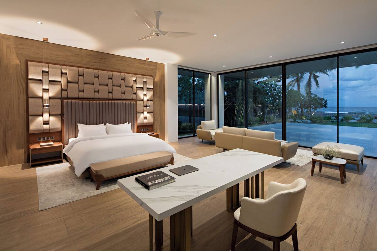 A modern bedroom with a large bed, a desk, and a view of the ocean.
