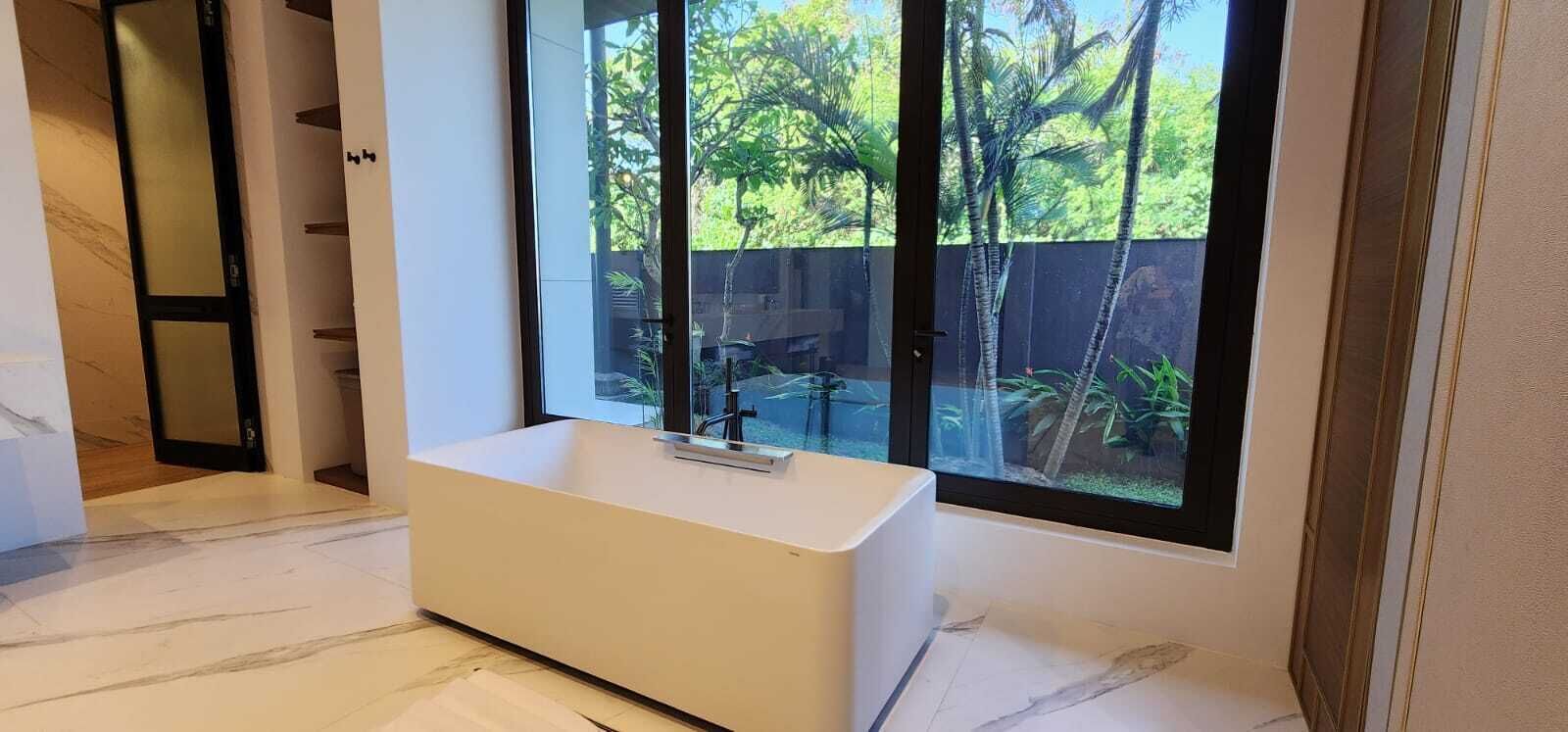 Um banheiro moderno com uma banheira grande, uma janela com vista para vegetação e piso de mármore.