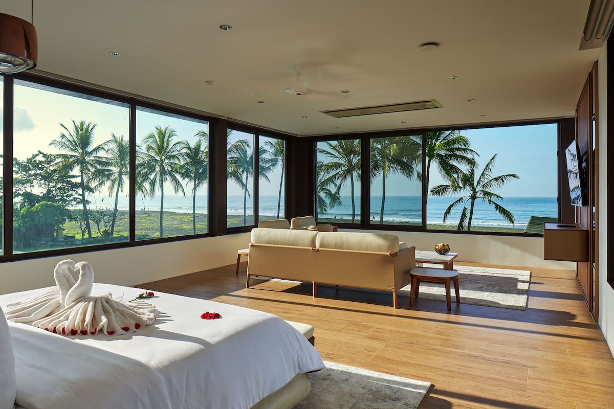 A modern bedroom with a large window overlooking palm trees and the ocean.