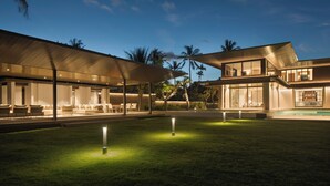 A modern house with a covered outdoor seating area, a swimming pool, and a well-lit lawn. - Saba Estate Luxury Villa Bali (Blahbatuh)