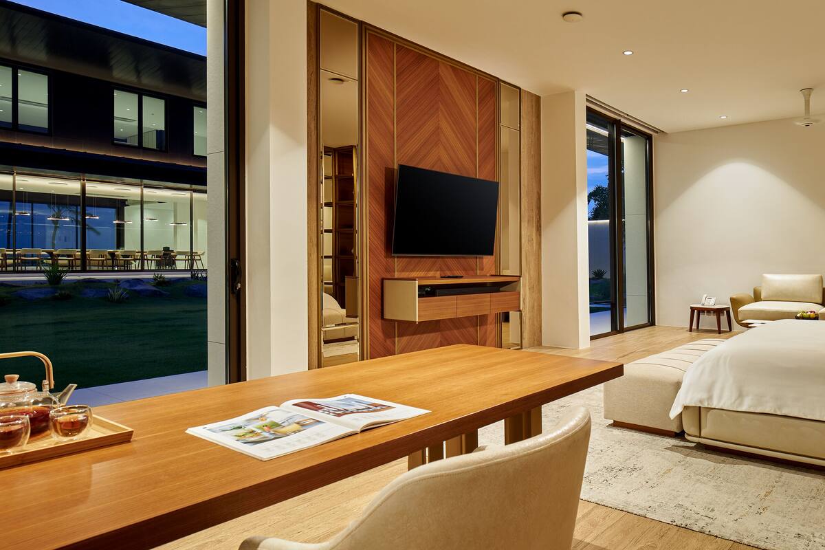 A modern hotel room with a large bed, a TV, a dining table with a tray of drinks, and a view of the outdoors.