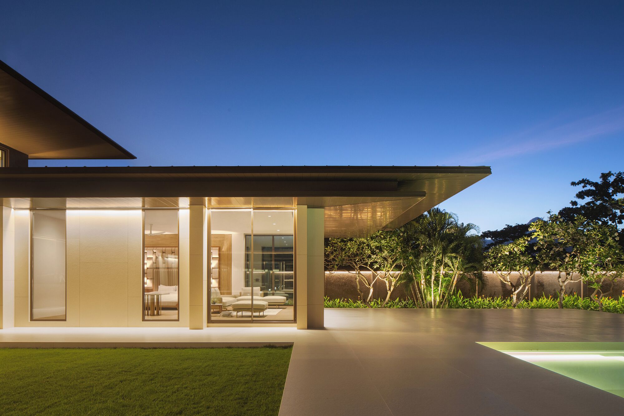 Une maison moderne avec une façade en verre, un toit plat et une pelouse bien entretenue.