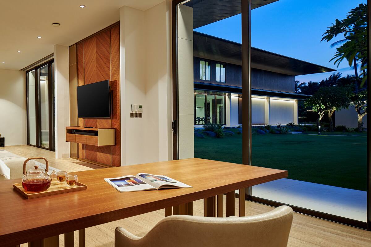A modern bedroom with a large bed, a TV, and a dining area with a view of the outdoors.