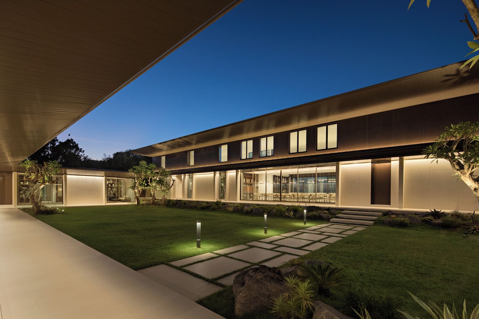 Una casa moderna con un patio amplio, un césped cuidado y un comedor con grandes ventanales.