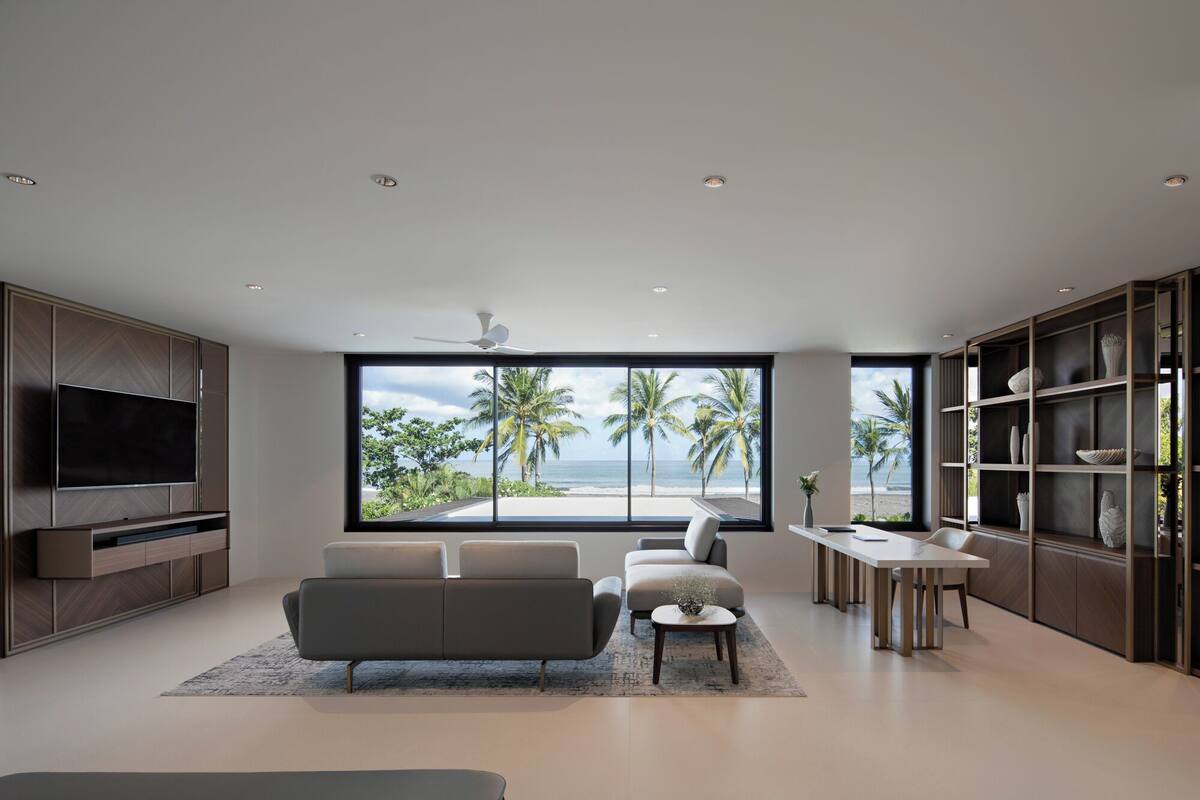 A modern living room with a large TV, comfortable seating, a dining area, and a view of the beach.