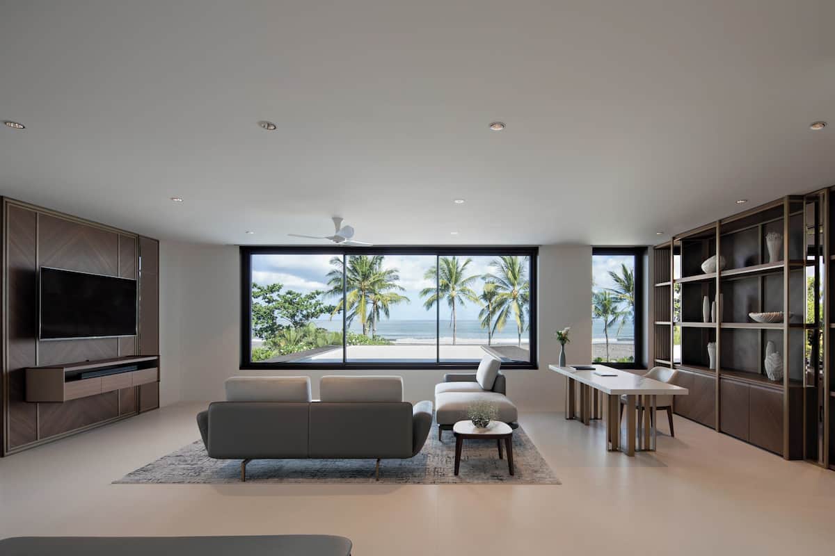 Una sala de estar moderna con un televisor grande, asientos cómodos, un comedor y vista a la playa.
