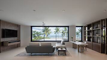 Una sala de estar moderna con un televisor grande, asientos cómodos, un comedor y vista a la playa.