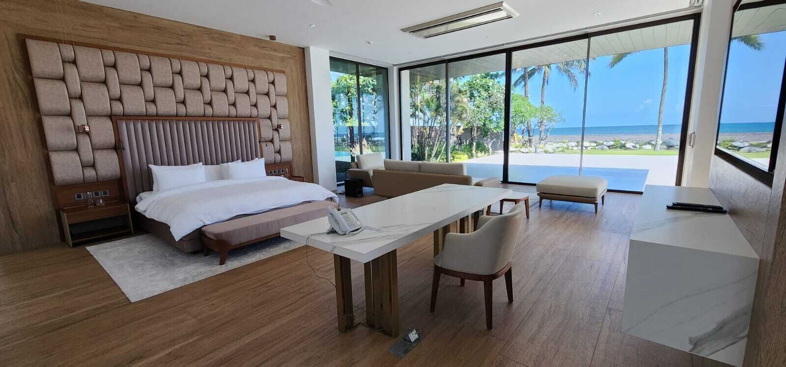 A modern bedroom with a large bed, a desk, and a view of the ocean.