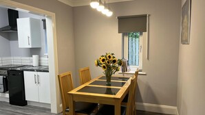 A kitchen with a dining table, chairs, a vase with sunflowers, and a window with blinds.