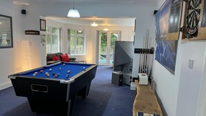 A pool table with balls, a dartboard, and a billiards cue rack in a room with a blue carpet.
