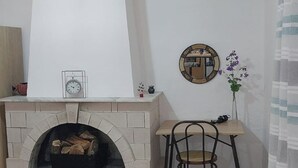 A fireplace with a clock and a mirror above it, a table with a chair, and a vase with flowers on the wall. - Lovely Studio in Strinilas with its own pool (Strinilas)