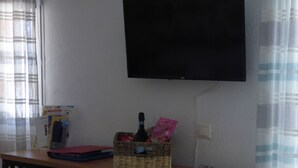 A room with a desk, a television mounted on the wall, and a basket containing a bottle and a book. - Lovely Studio in Strinilas with its own pool (Strinilas)