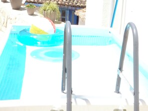 Uma piscina com escada, um brinquedo flutuante e plantas em vasos.