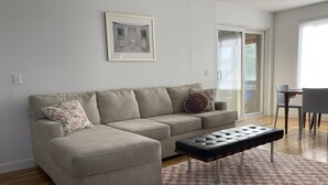 Un salon avec un canapé beige, un pouf noir et un tapis à motifs.