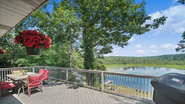 A wooden deck with a table and chairs, overlooking a lake with trees and a grassy area. - Available Sept 7-10 & 13-17- Private Mini Resort w Indoor Pool & Sauna (West Olive)