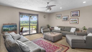 A spacious living room with a large sliding glass door leading to a balcony, a ceiling fan, and a fish tank. - Available Sept 7-10 & 13-17- Private Mini Resort w Indoor Pool & Sauna (West Olive)