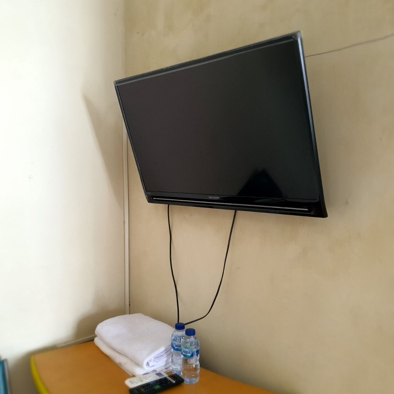 Ein an der Wand befestigter Fernseher mit Fernbedienung und zwei Wasserflaschen auf einem kleinen Tisch darunter.