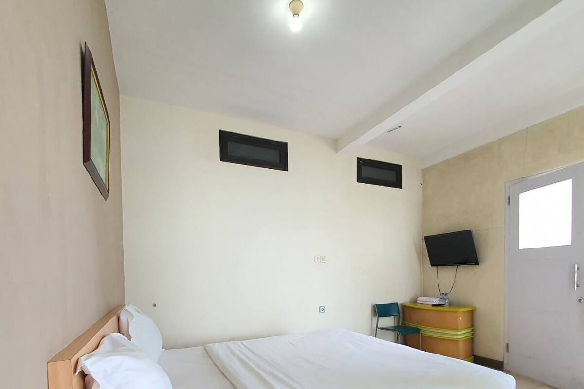 A bedroom with a bed, a television on a stand, a door, and a small window.