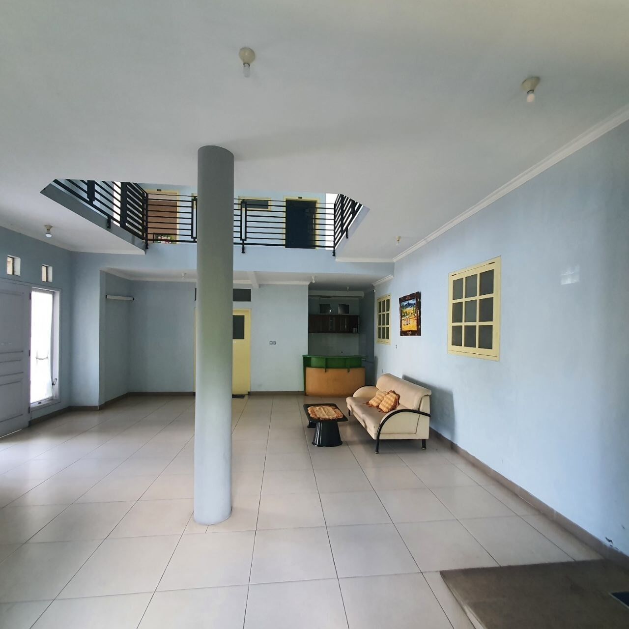A spacious living area with a high ceiling, a central column, a sofa, a small table, and a kitchen area in the background.