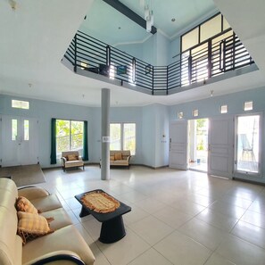 A spacious living area with a high ceiling, a balcony, and large windows allowing natural light. - Candi Panggung Family Guest House Syariah (Malang)